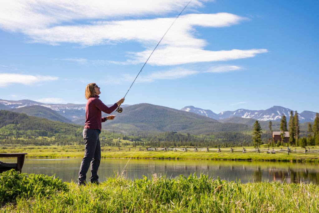 A woman casts with a fishing pole at a mountain pond.