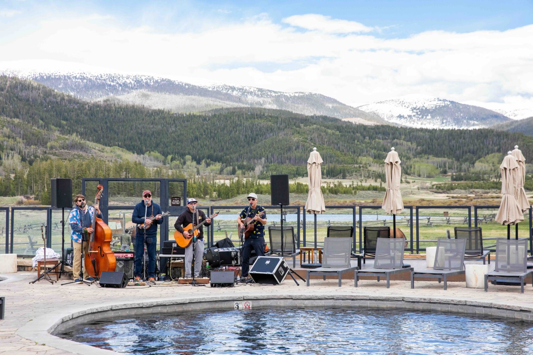 A band plays outdoors with a swimming pool in the foreground and mountains in the background