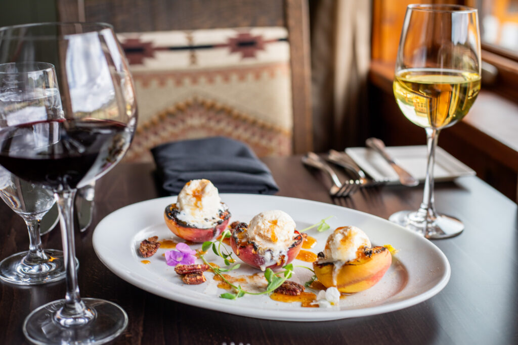 Grilled peach and ice cream dessert with glasses of wine