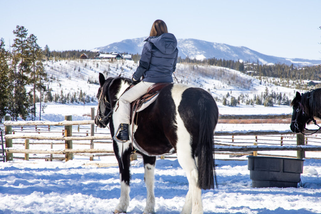 Woman on horseback looks out at snowy mountain landscape