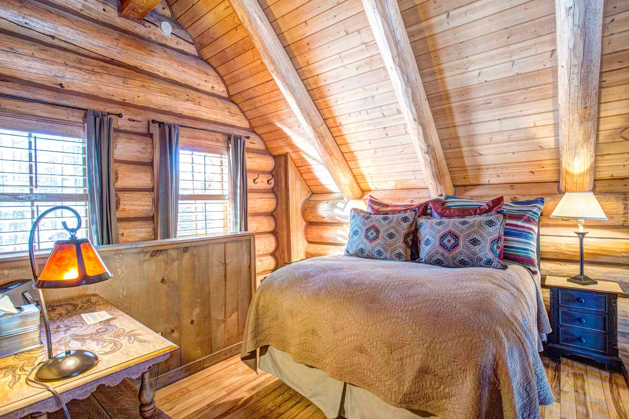 Warm log cabin bedroom with rustic decor, wooden walls, and cozy bedding at Devil's Thumb Ranch.