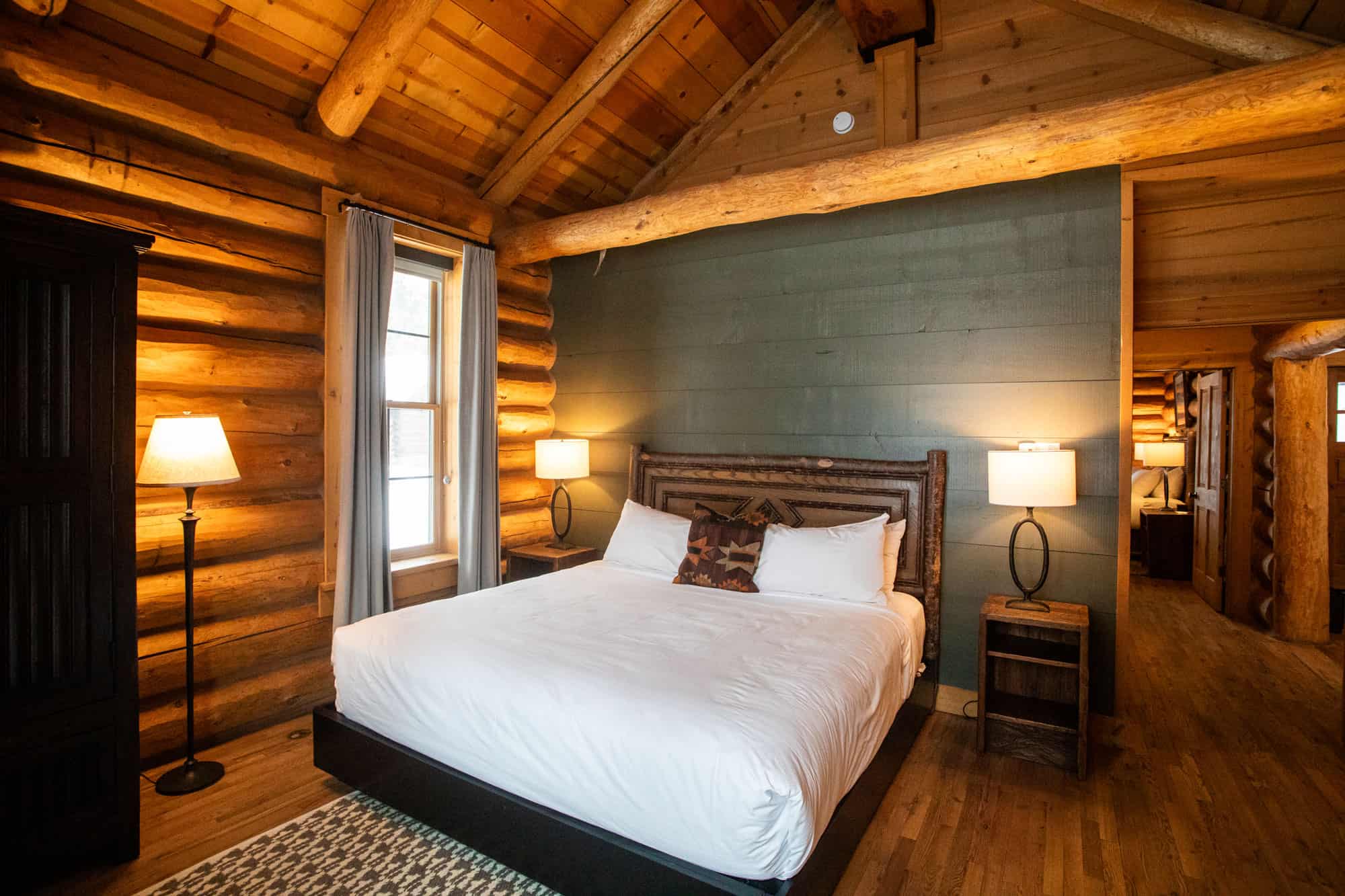 Rustic bedroom with wooden logs, cozy bed, and warm lighting at Devil's Thumb Ranch.