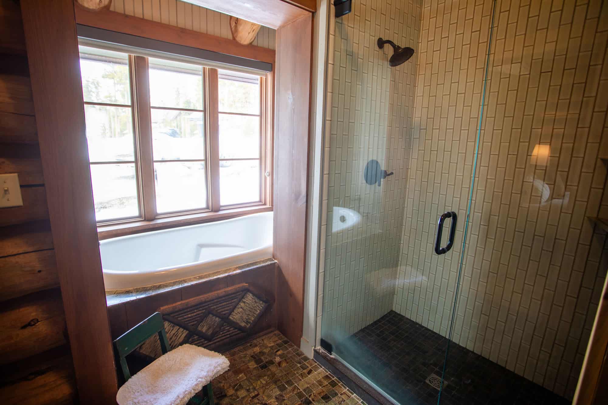 Cozy bathroom with a walk-in shower and a bathtub by the window at Devil's Thumb Ranch.