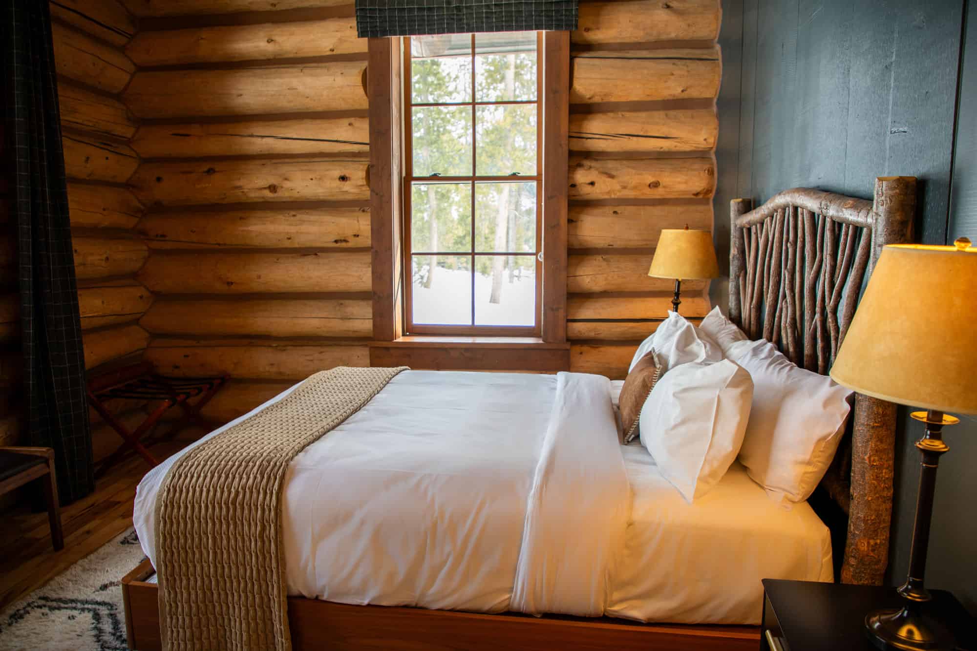 Comfortable rustic bedroom with wooden log walls and large window overlooking nature.