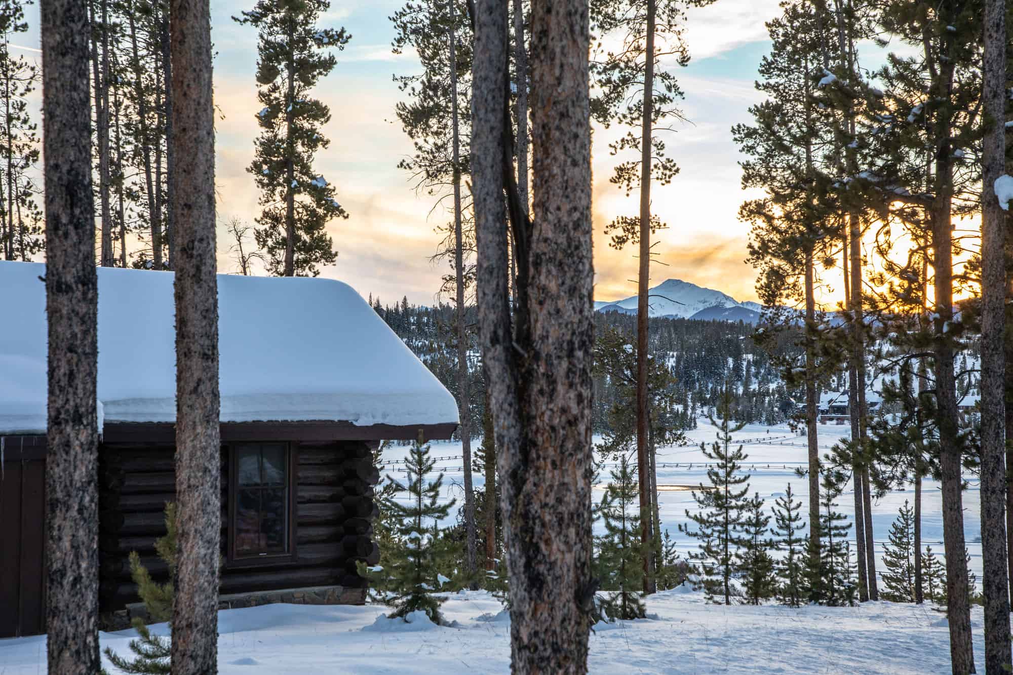 Cozy log cabin surrounded by snow-covered trees at sunset in a winter landscape.