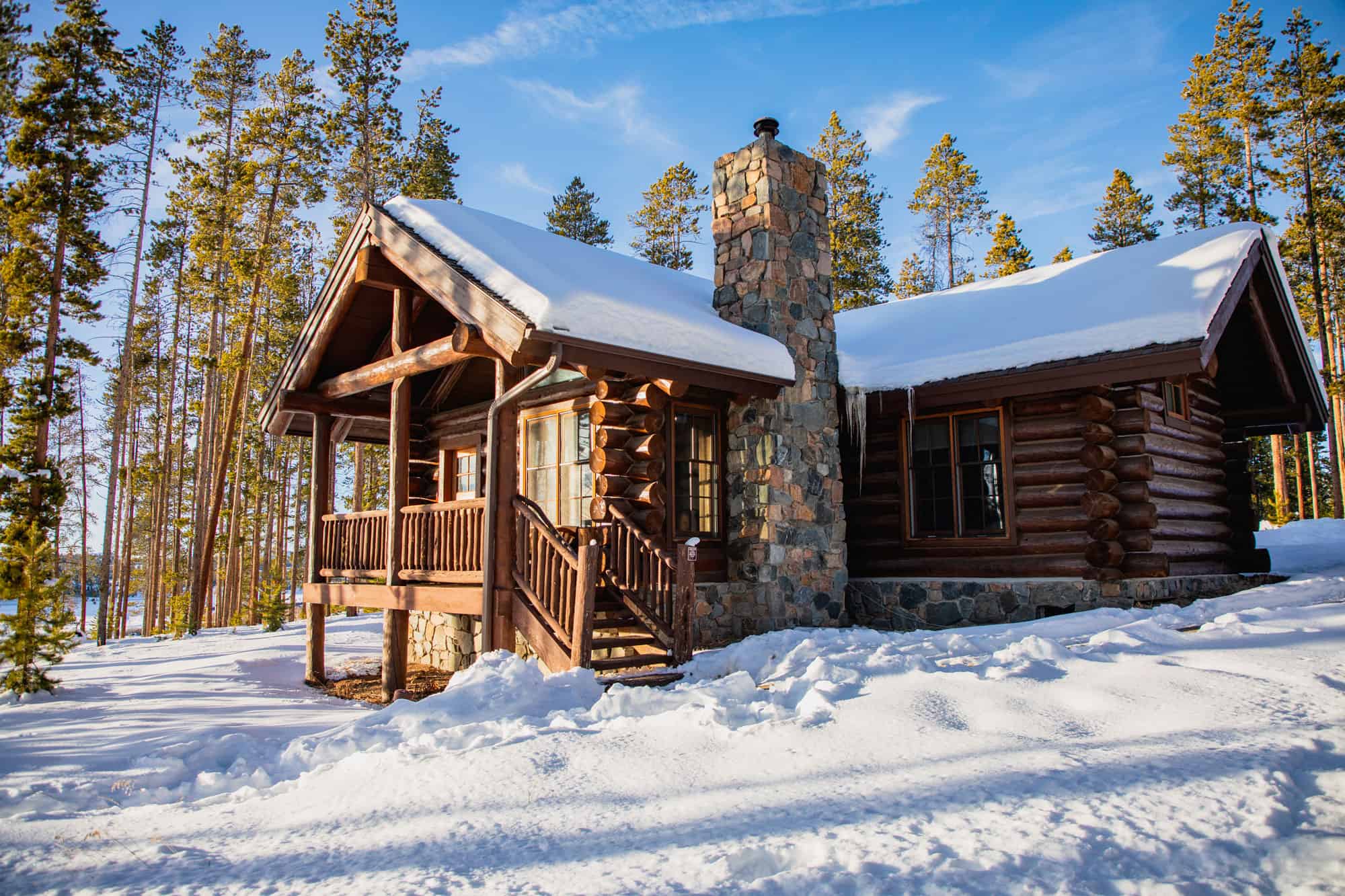Rustic log cabin with stone chimney in snowy forest setting at Devil's Thumb Ranch.