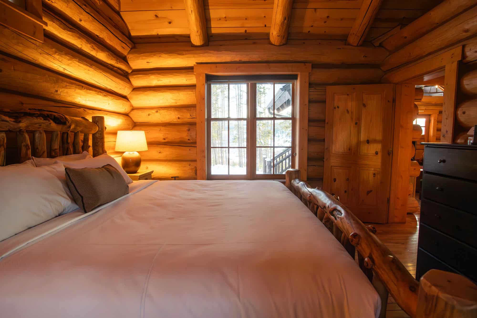 Rustic log cabin bedroom with a large bed, wooden walls, and natural light from a window.