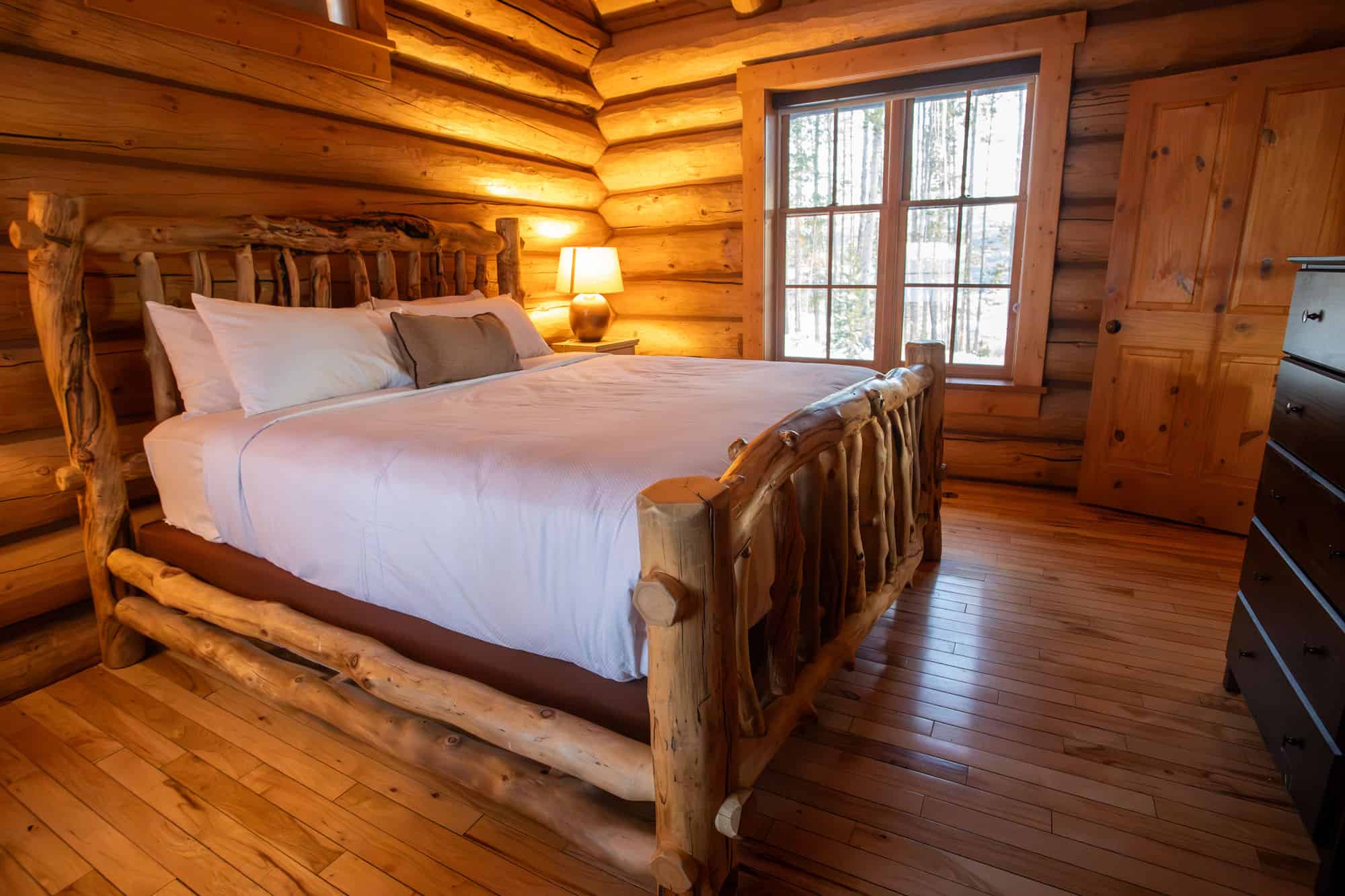 Cozy log cabin bedroom with wooden furniture and large window at Devil's Thumb Ranch.