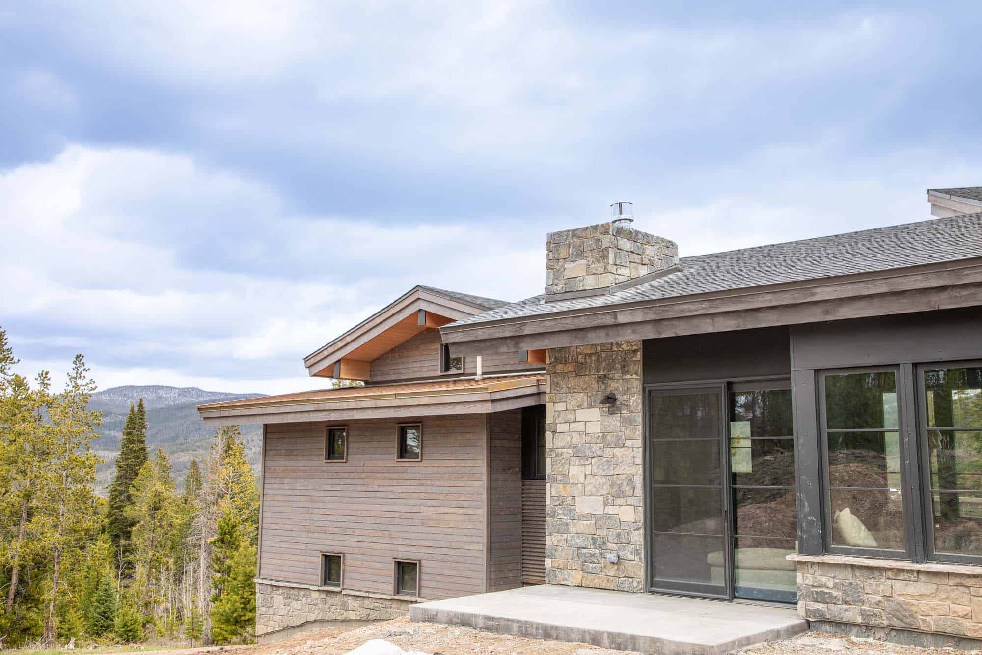 Contemporary mountain lodge with stone and wood exterior, large windows, and scenic forest views.