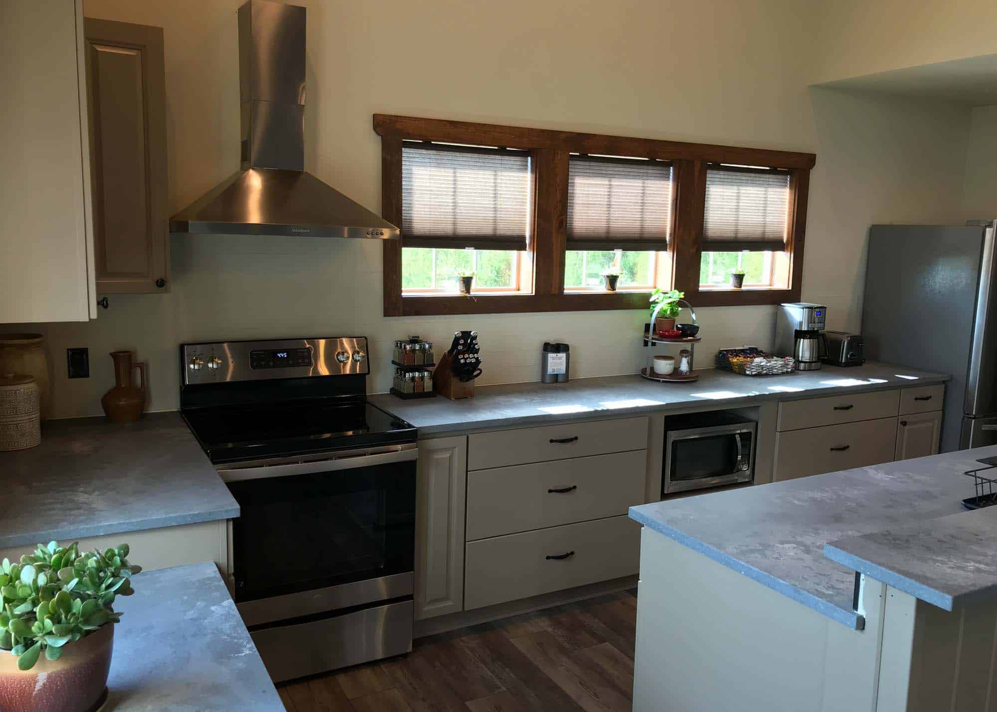 Modern kitchen with gray cabinets, stainless steel stove, microwave, and window view.
