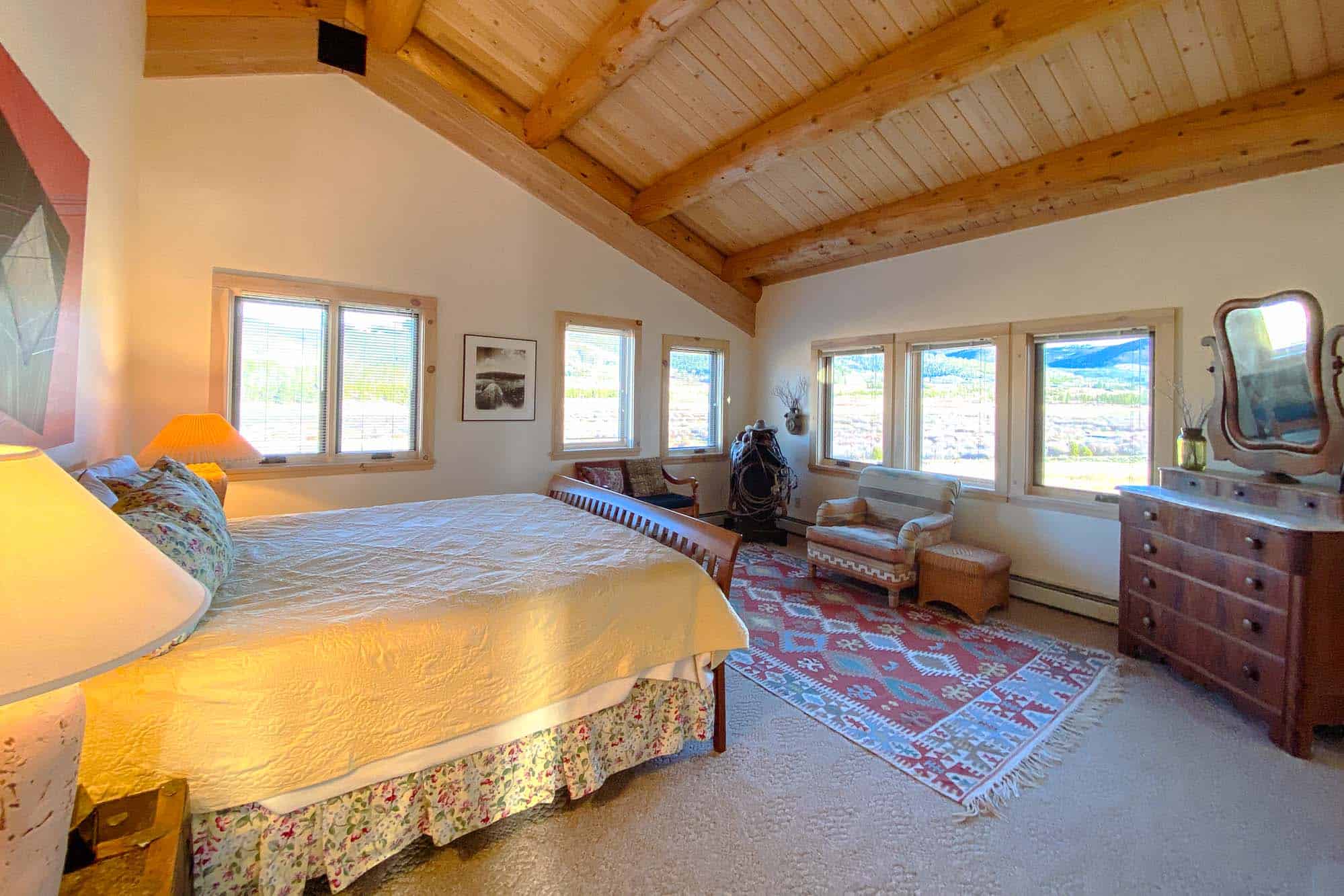 Interior view of a cozy mountain bedroom with a large bed, wooden ceiling, and scenic windows.