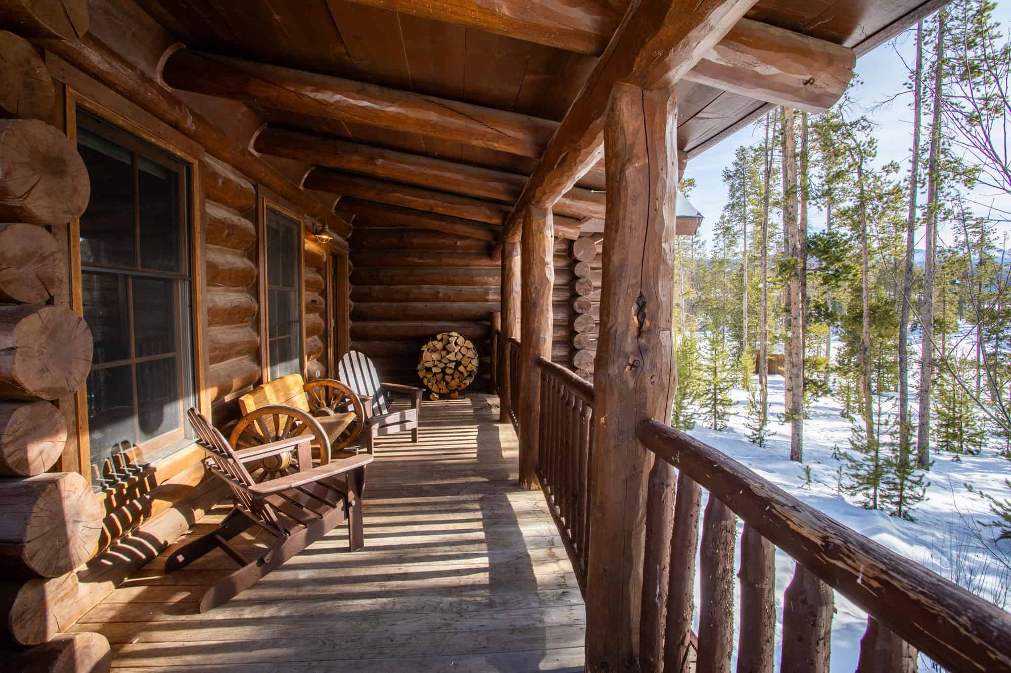 Cozy log cabin porch with wooden chairs overlooking snowy forest landscape at Devil's Thumb Ranch Re.
