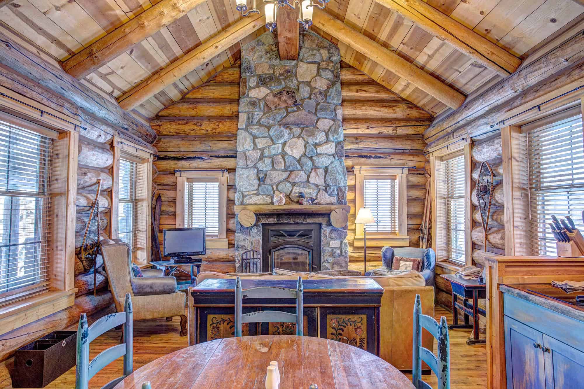 Warm log cabin living room with stone fireplace and rustic wooden decor.