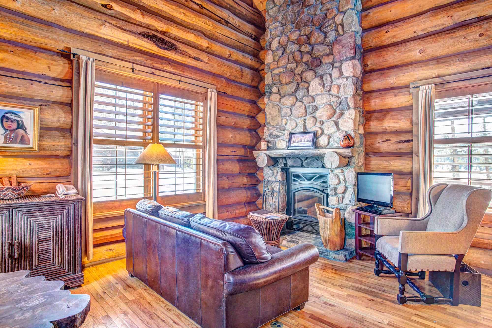 Cozy log cabin living room with stone fireplace, leather sofa, and wooden accents at Devil's Thumb R.
