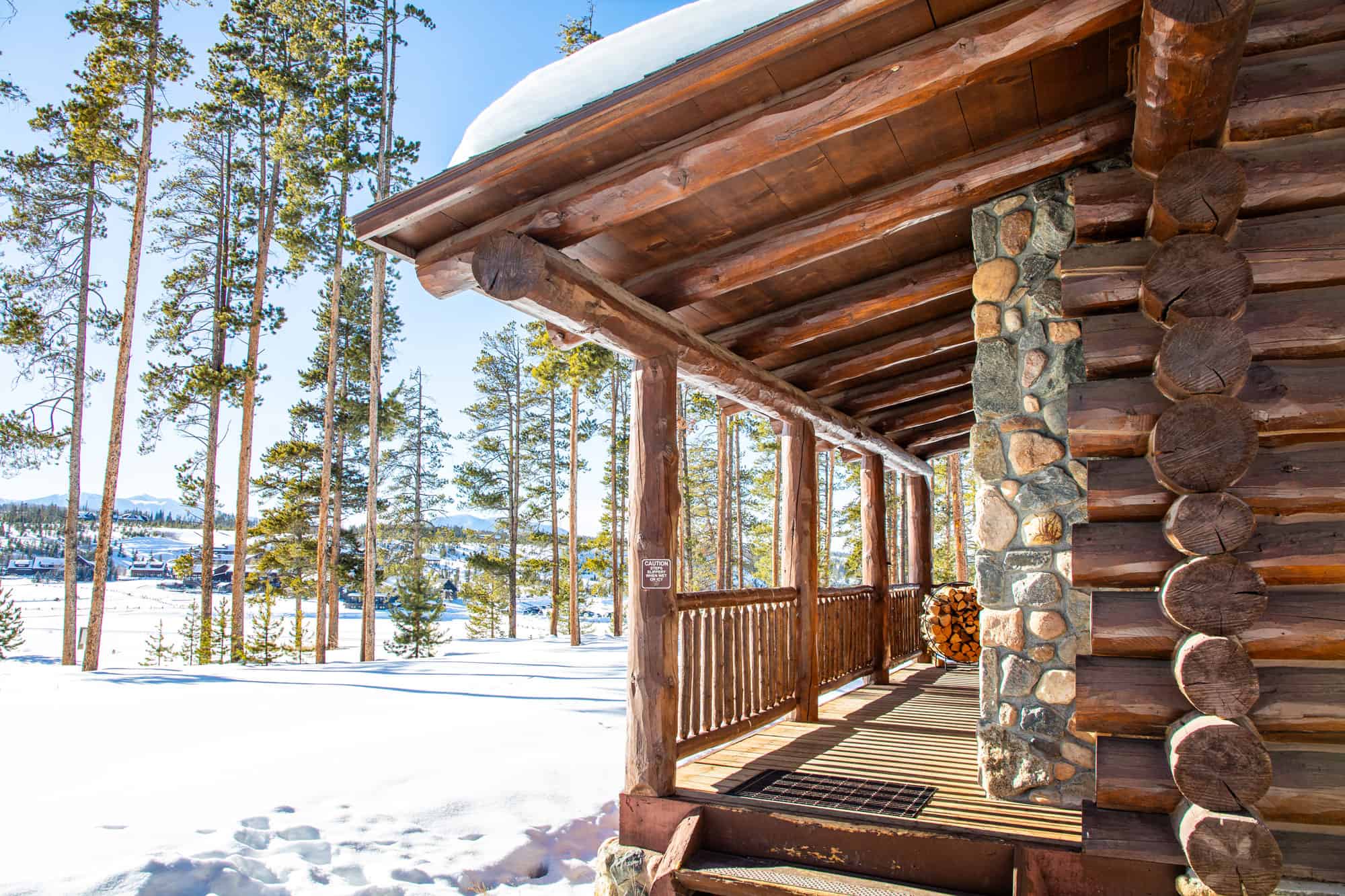 Cozy log cabin porch at Devil's Thumb Ranch Resort in winter with snow-covered landscape.