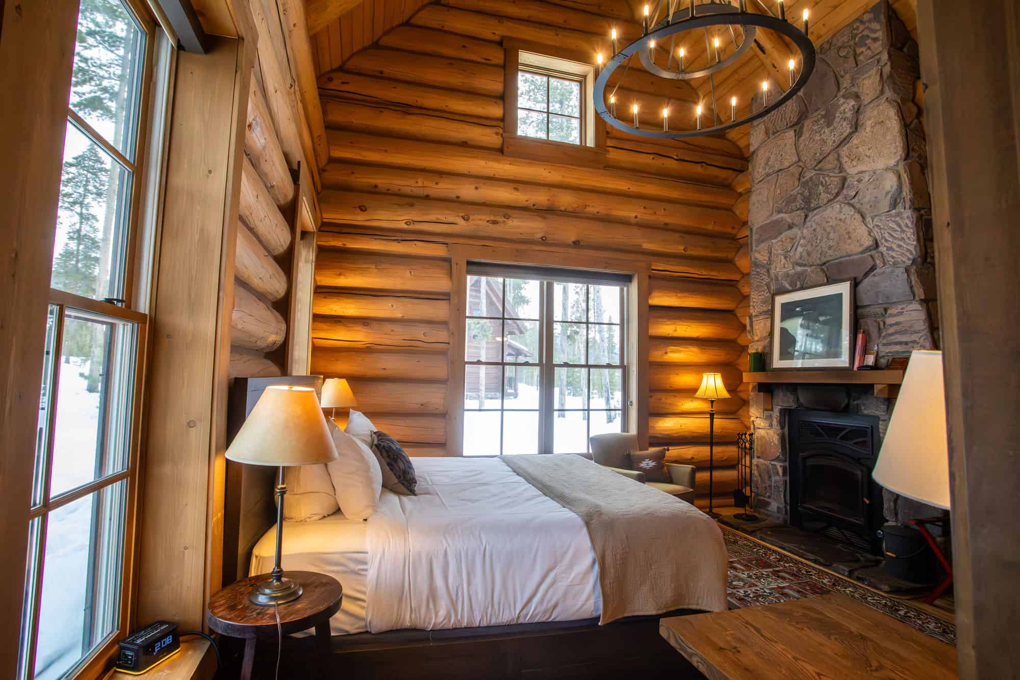 Cozy bedroom with wooden log walls, large windows, and a stone fireplace at Devil's Thumb Ranch Reso.