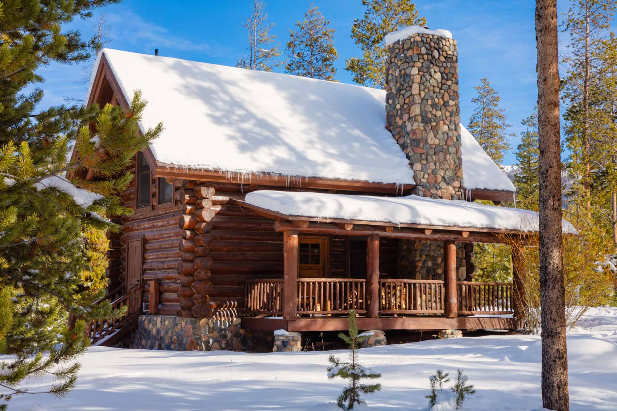 Cozy log cabin at Devil's Thumb Ranch in winter with snow-covered roof and surrounding trees.