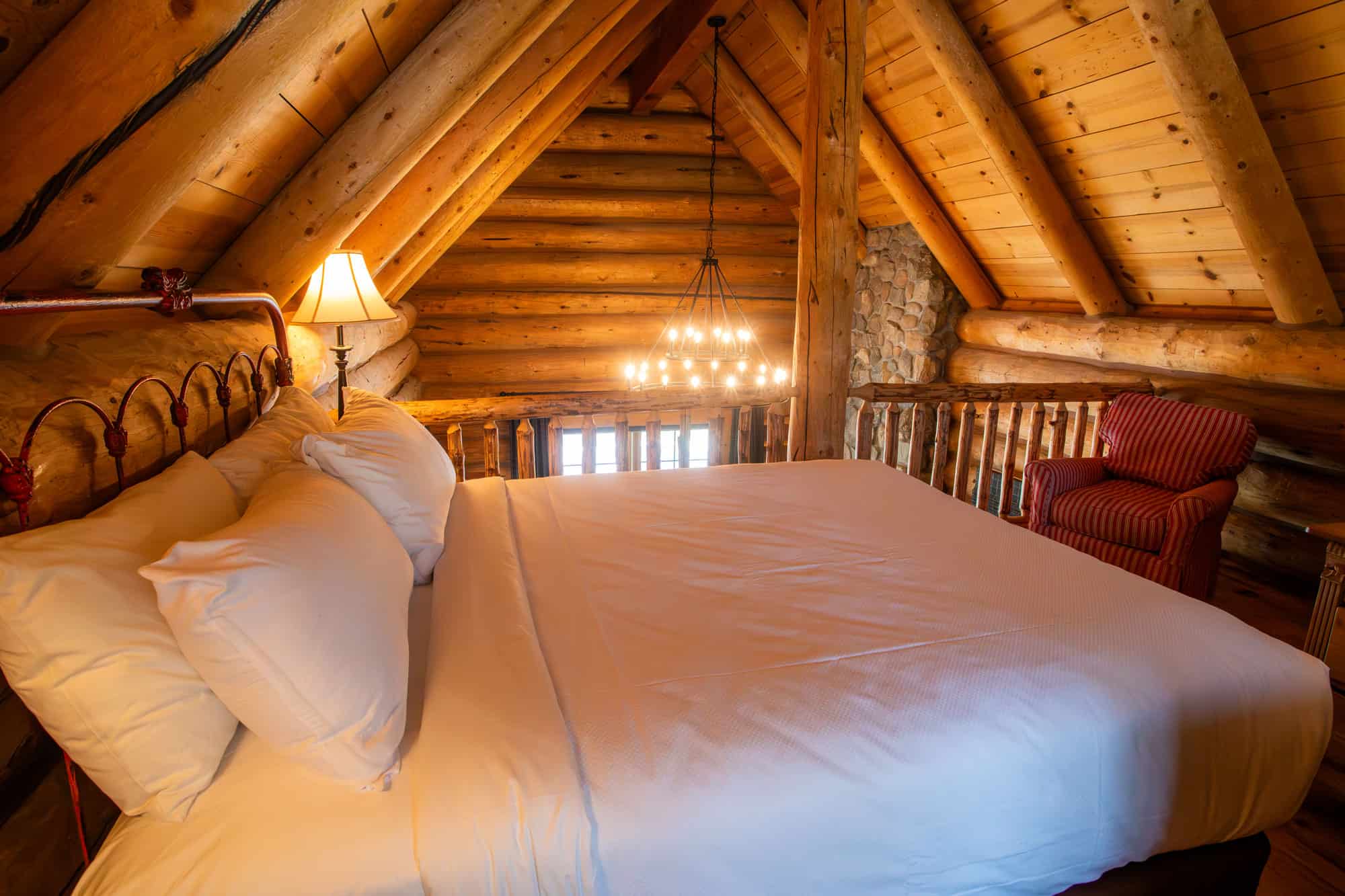 Charming rustic bedroom with a large bed, wooden beams, and warm lighting in a log cabin setting.