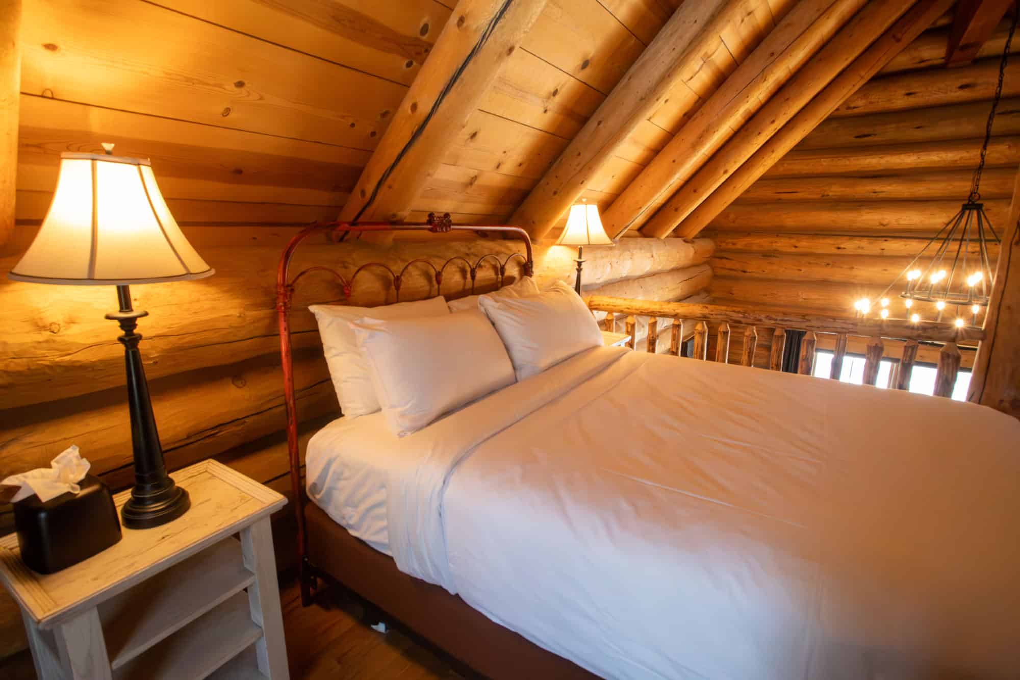 Warm log cabin bedroom at Devil's Thumb Ranch with wooden walls and soft lighting.