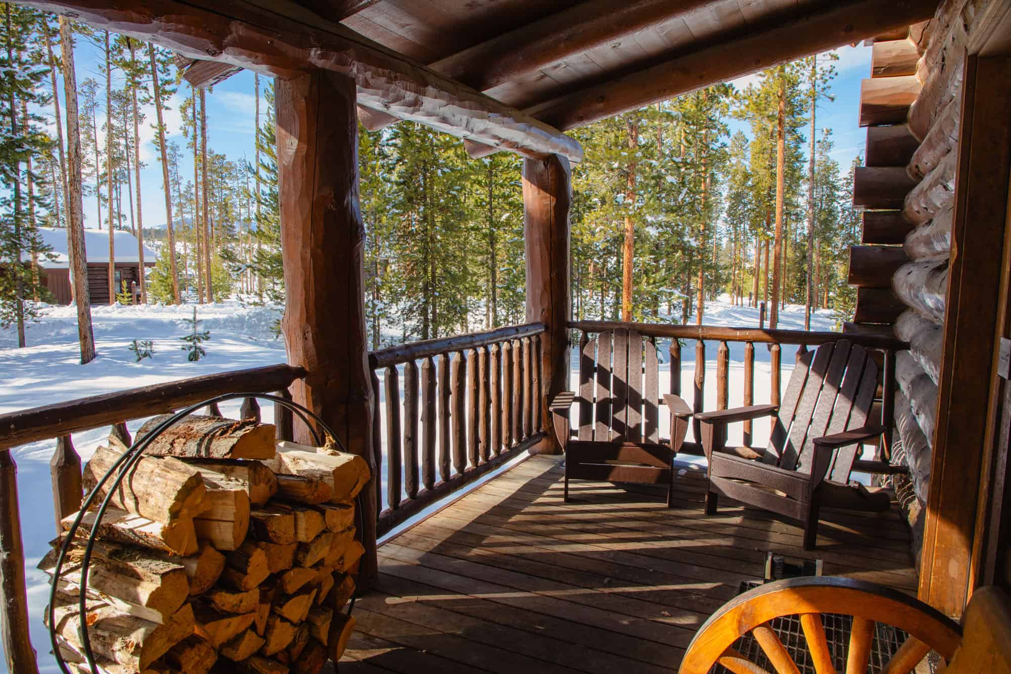 Cozy cabin porch at Devil's Thumb Ranch with wooden chairs and a view of snow-covered trees.