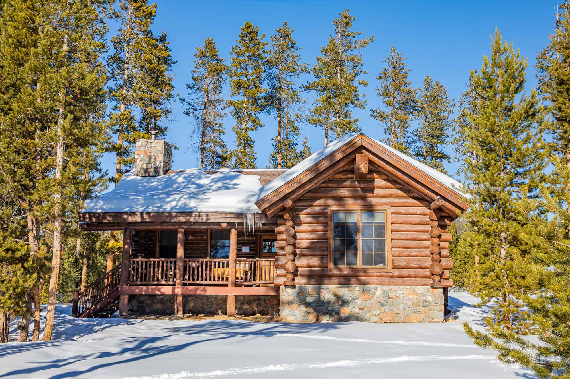Cabin at Devil's Thumb Ranch Resort & Spa surrounded by snow and tall pine trees.