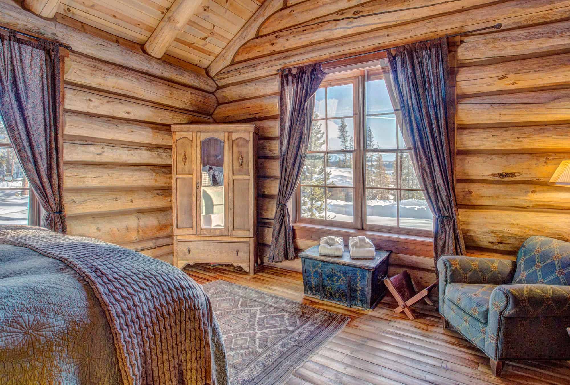 Charming log cabin bedroom with rustic wooden walls, large windows, and cozy furnishings at Devil's.