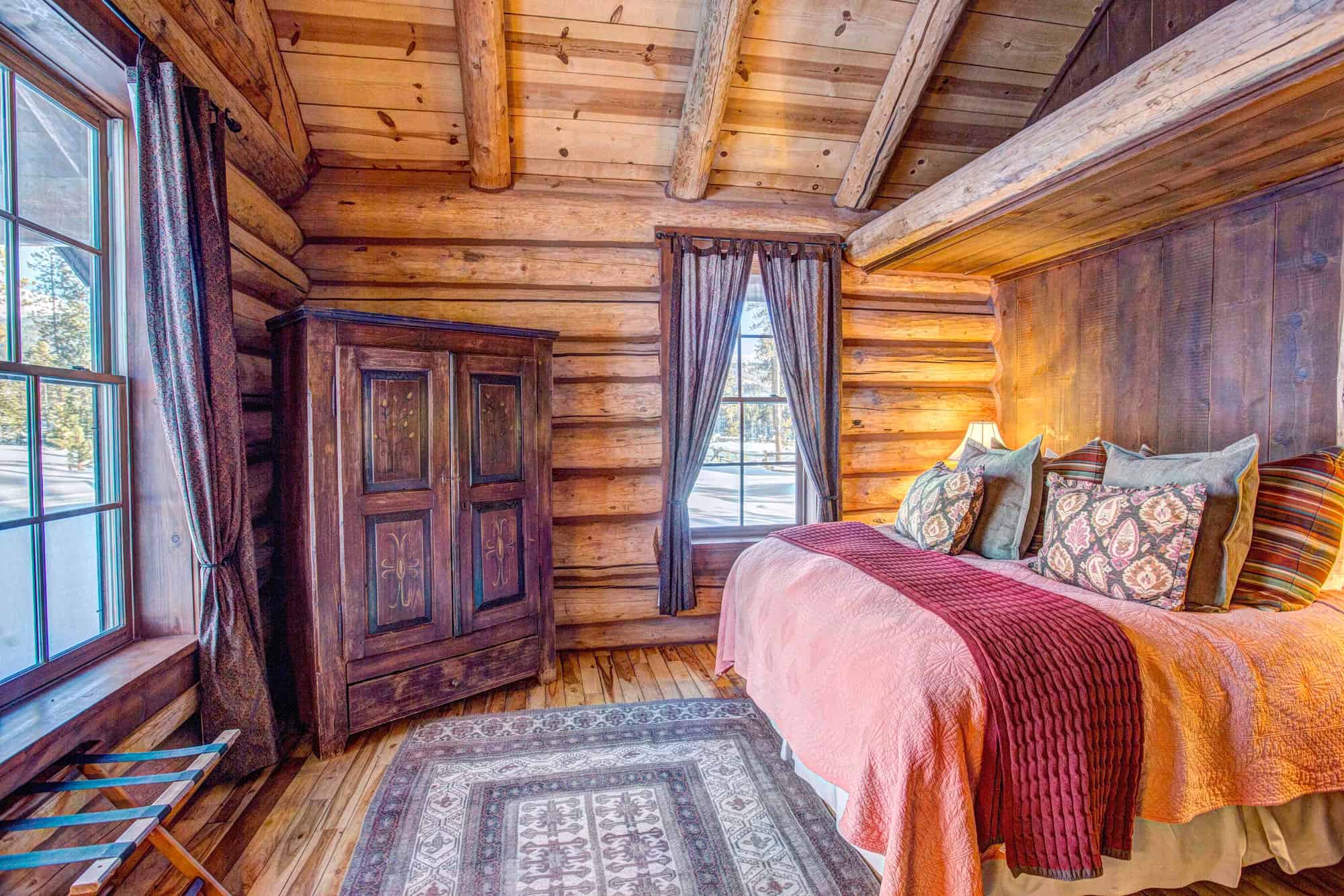 Rustic log cabin bedroom with wooden walls, large windows, and cozy bedding at Devil's Thumb Ranch.