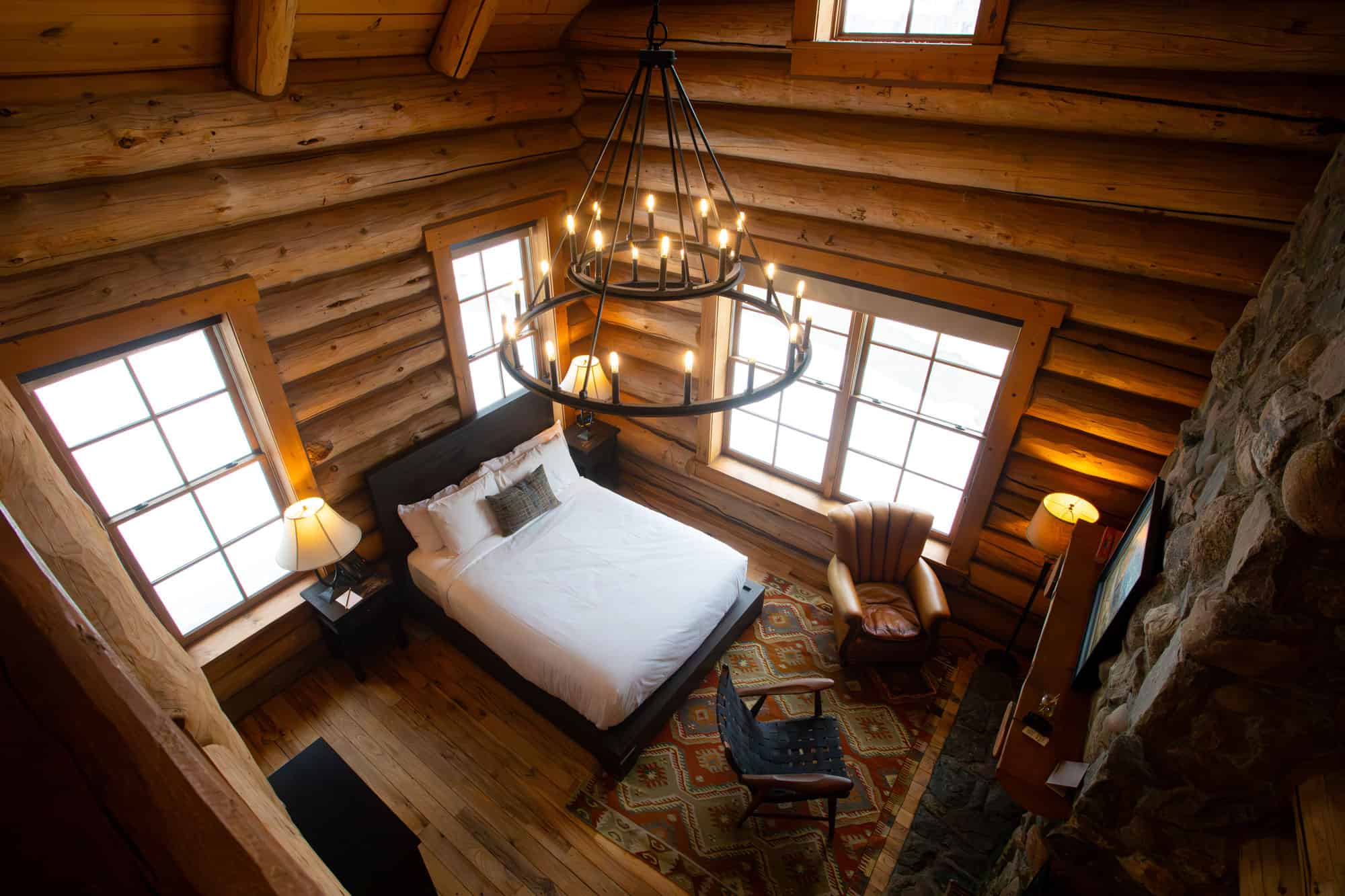 Interior view of a rustic log cabin bedroom with a large bed, wooden walls, and a chandelier.