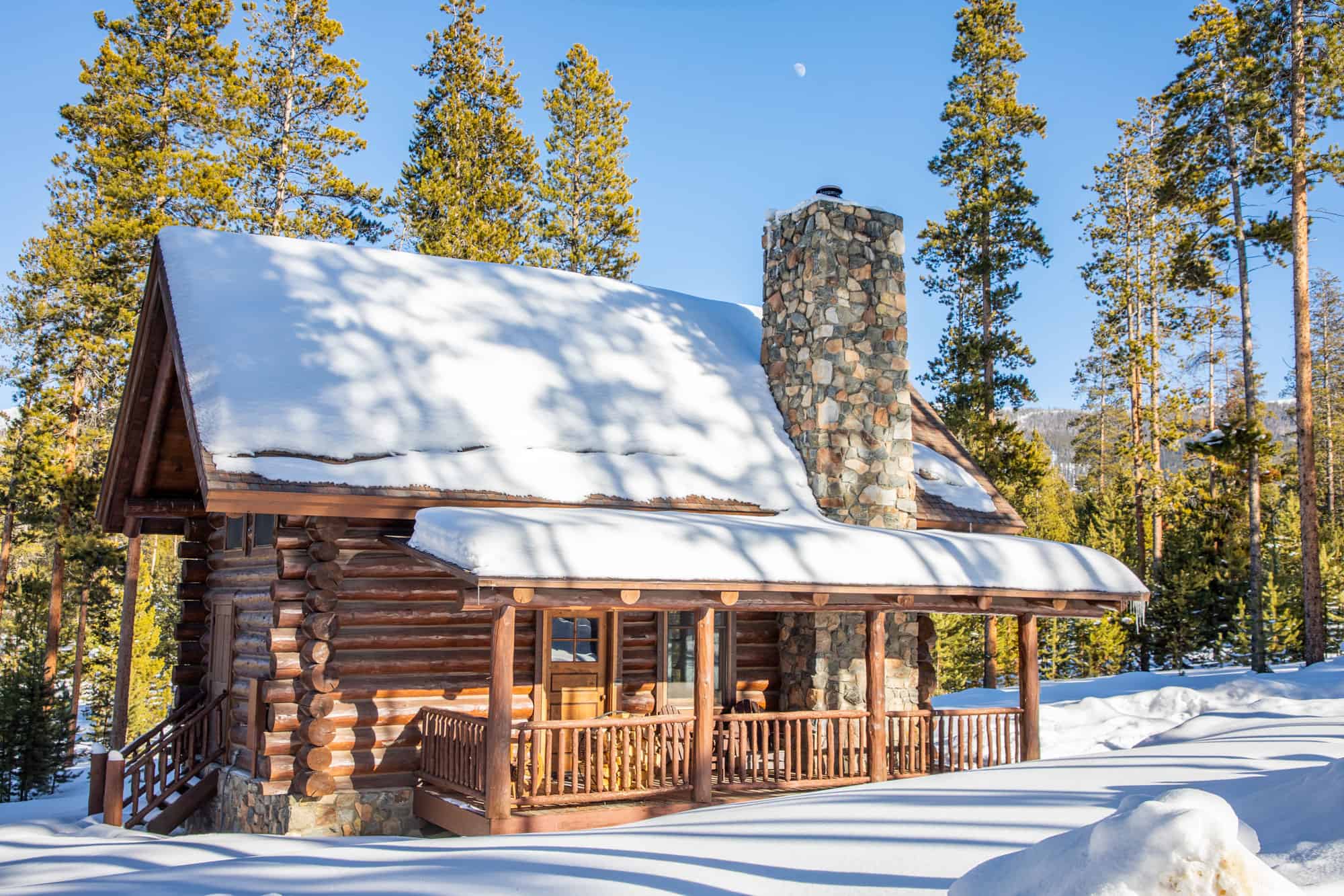 Cabin at Devil's Thumb Ranch covered in snow with tall pine trees in the background.
