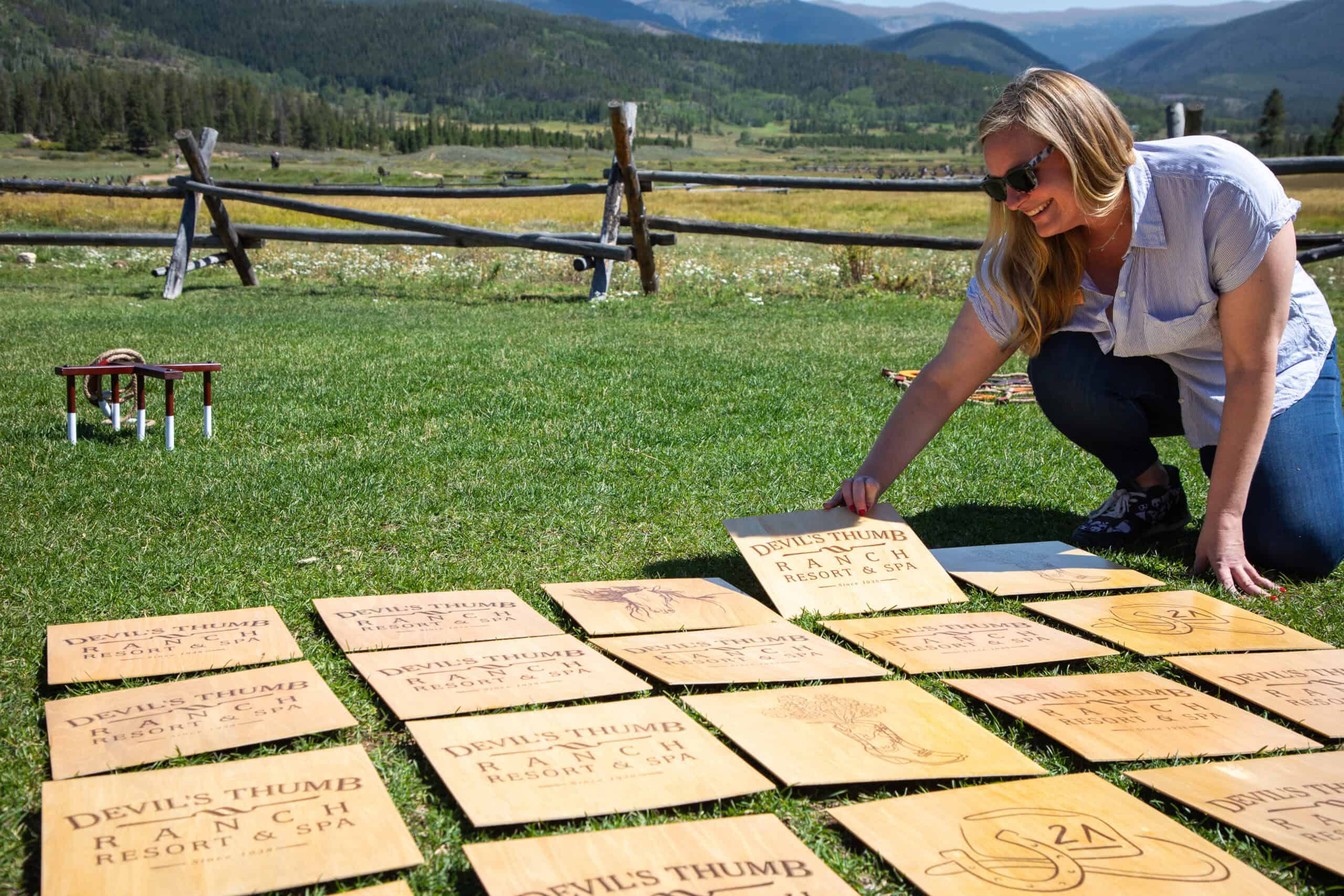 Woman arranging wooden signs outdoors at Devil's Thumb Ranch.