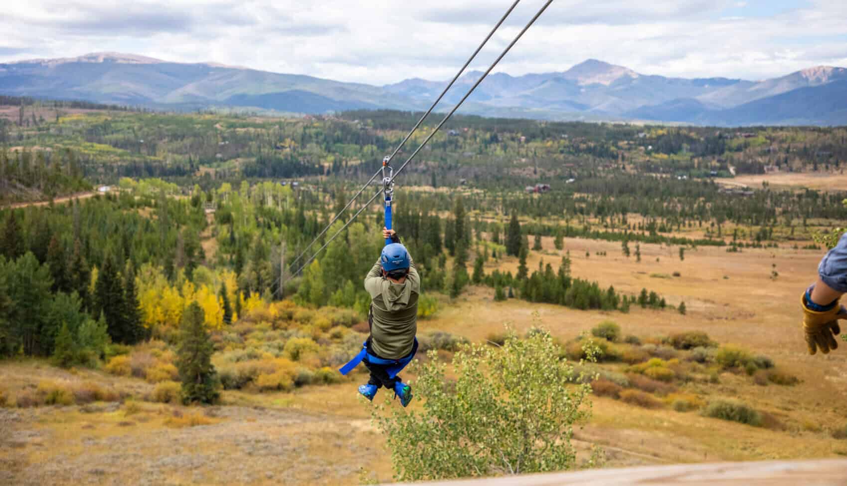 Person zip lining over scenic mountain landscape at Devil's Thumb Ranch Resort & Spa.