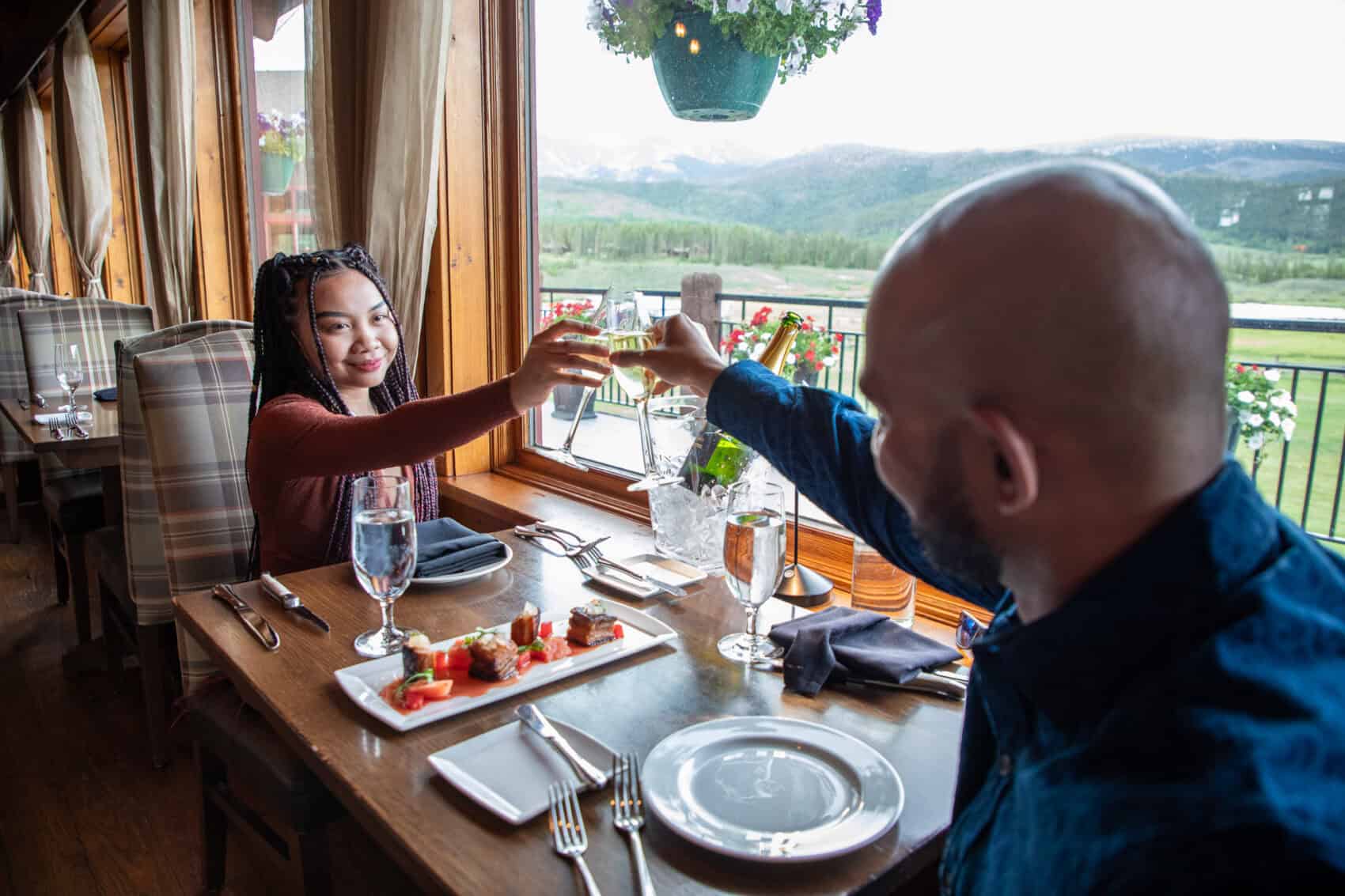 Two guests sharing a toast at a scenic mountain-view restaurant.