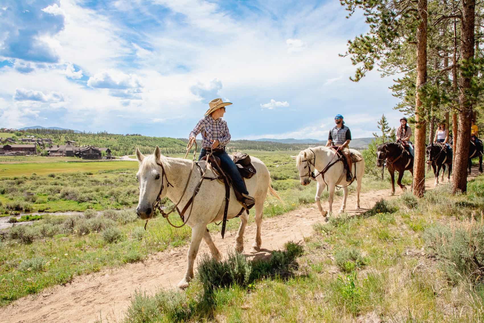 Group of people horseback riding through scenic landscape at Devil's Thumb Ranch.