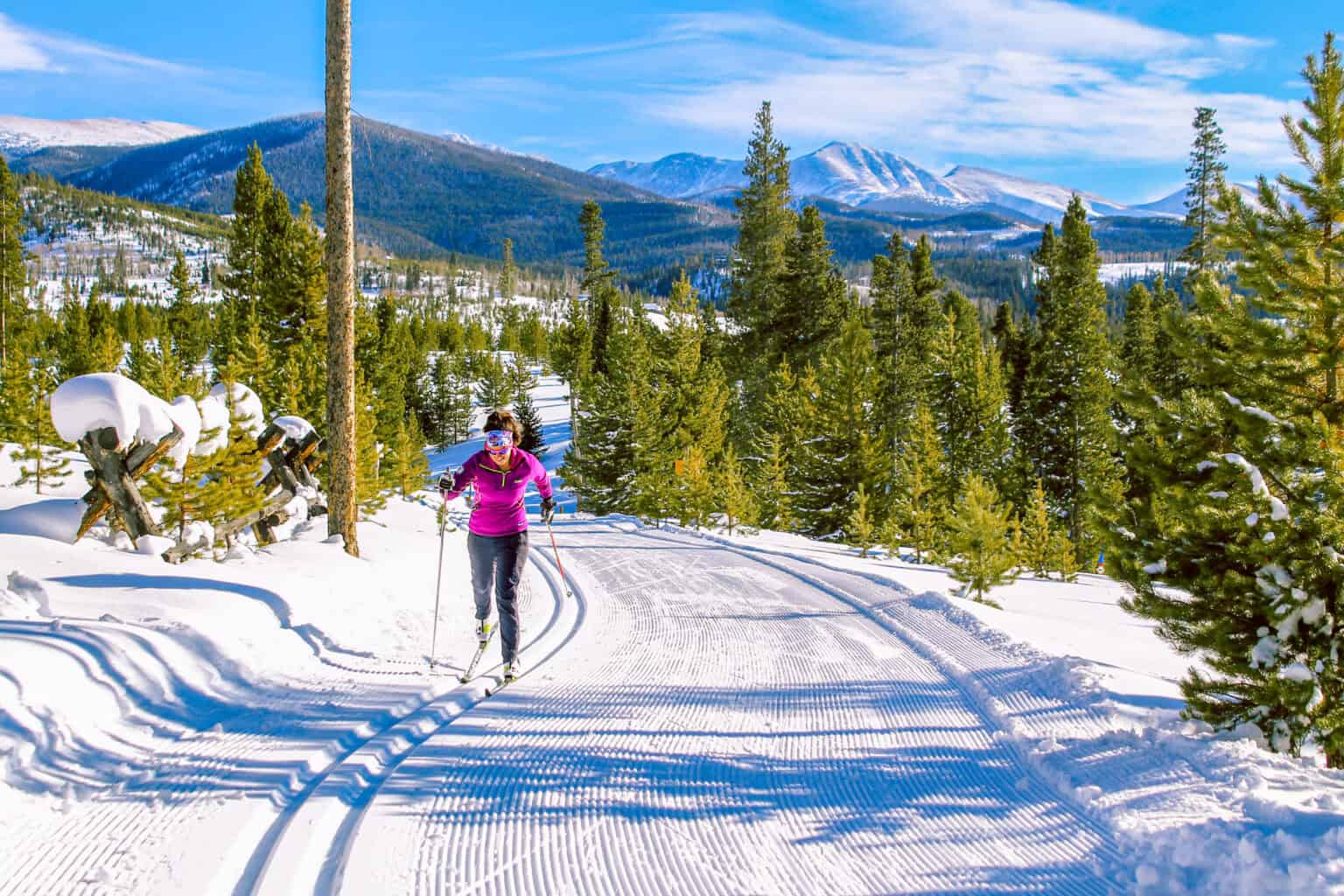 Woman skiing on groomed trail at Devil's Thumb Ranch in snowy mountain landscape.