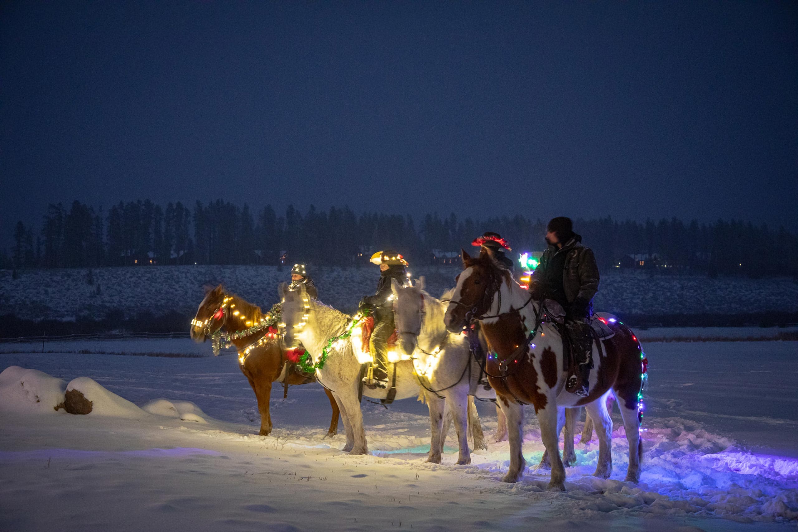 People riding horses on snow with Christmas lights at Devil's Thumb Ranch.