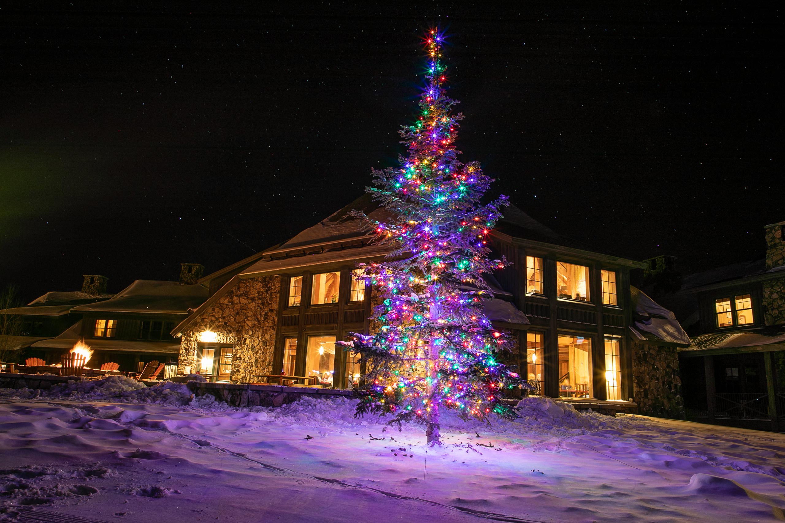 Colorful Christmas tree illuminated outside Devil's Thumb Ranch Resort at night.