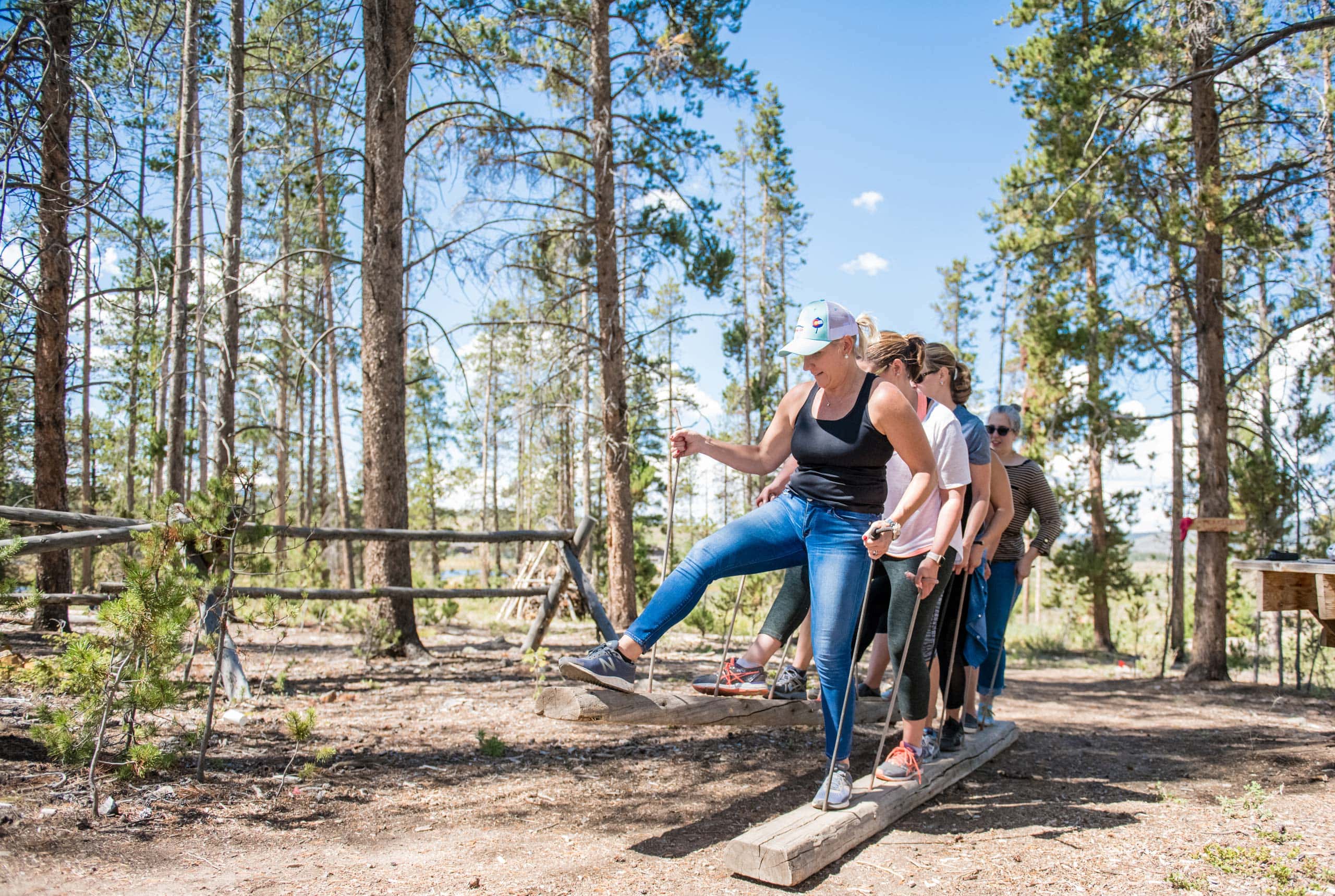 Group of people balancing on a wooden beam in a forest setting.