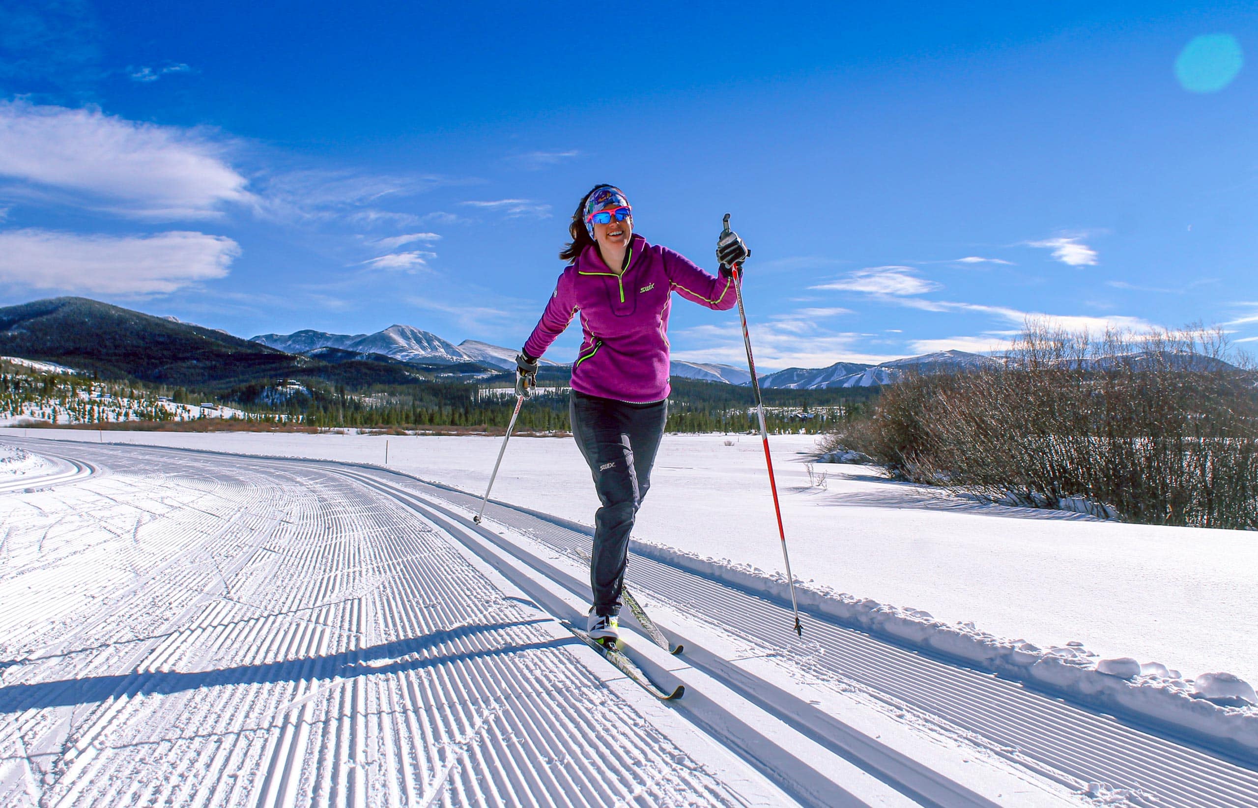 Woman cross-country skiing in snowy landscape with mountains in background.