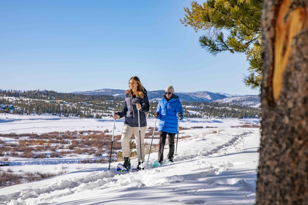Two women snowshoe on a mountain ridge