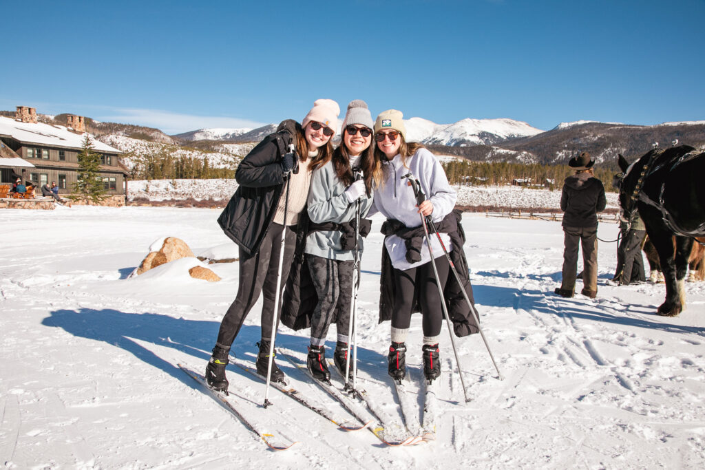 Three cross-country skiers stand close together smiling for the photo